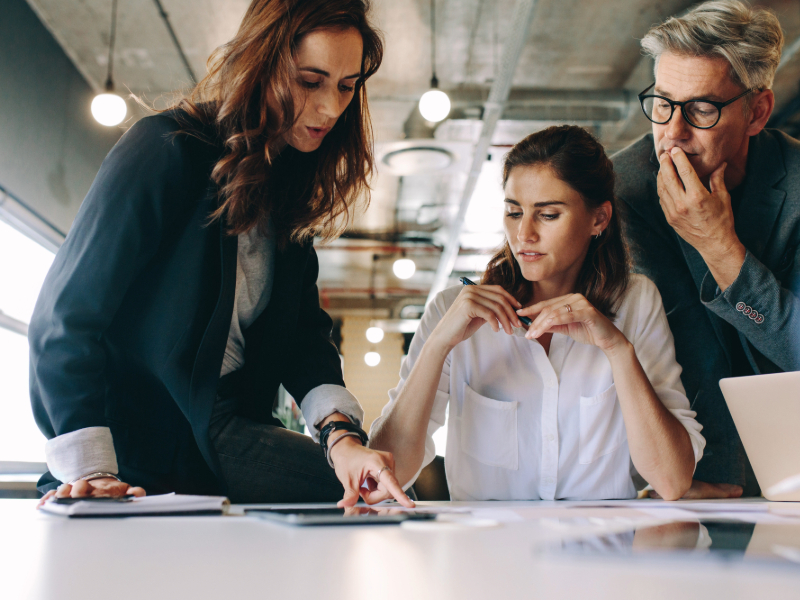 Professional women analyzing documents on a table during a work meeting, while collaborating with a colleague in a modern office.