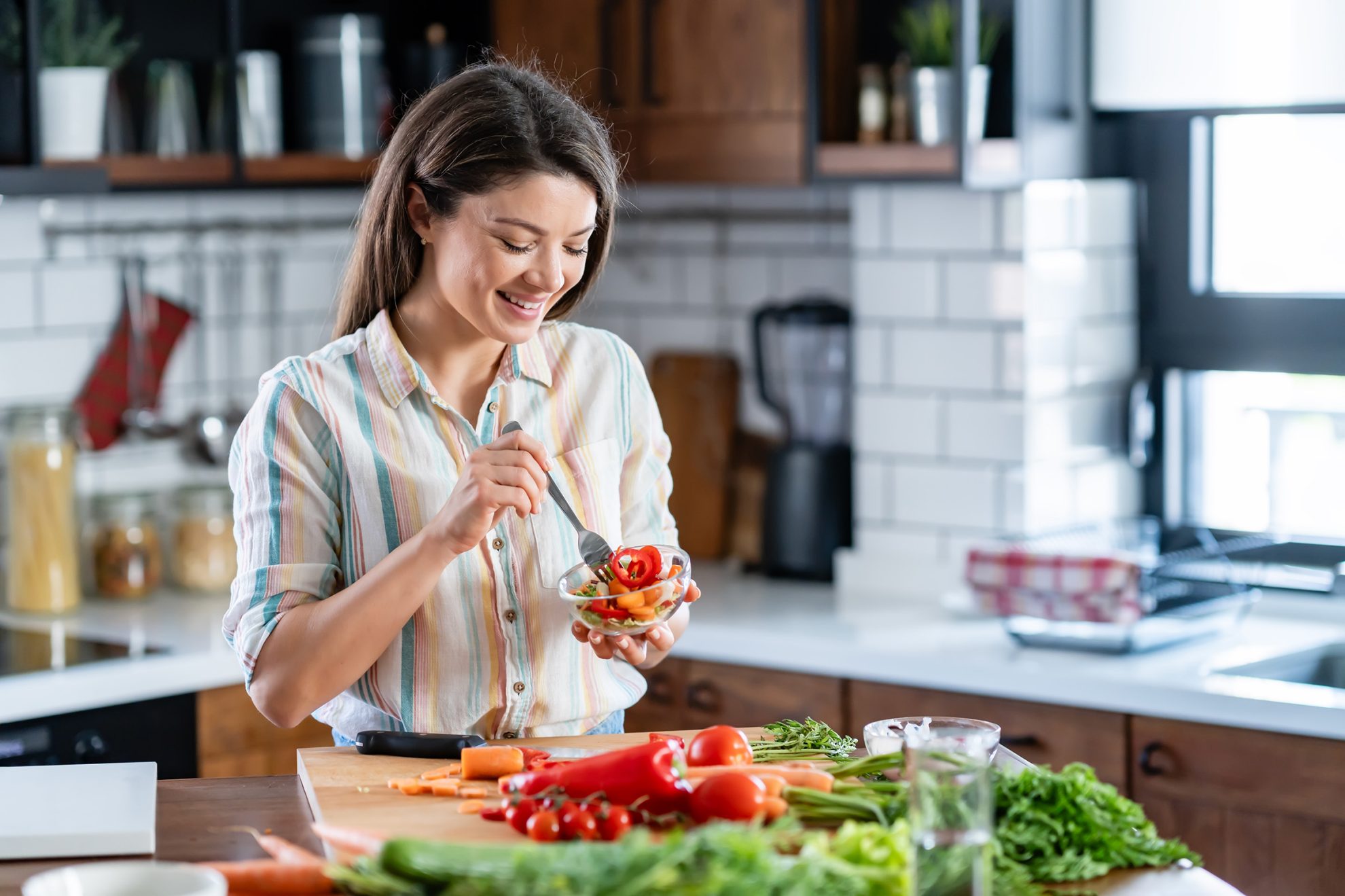 2480446627 A young pretty cheerful woman is preparing a healthy various vegetable-based meal at home