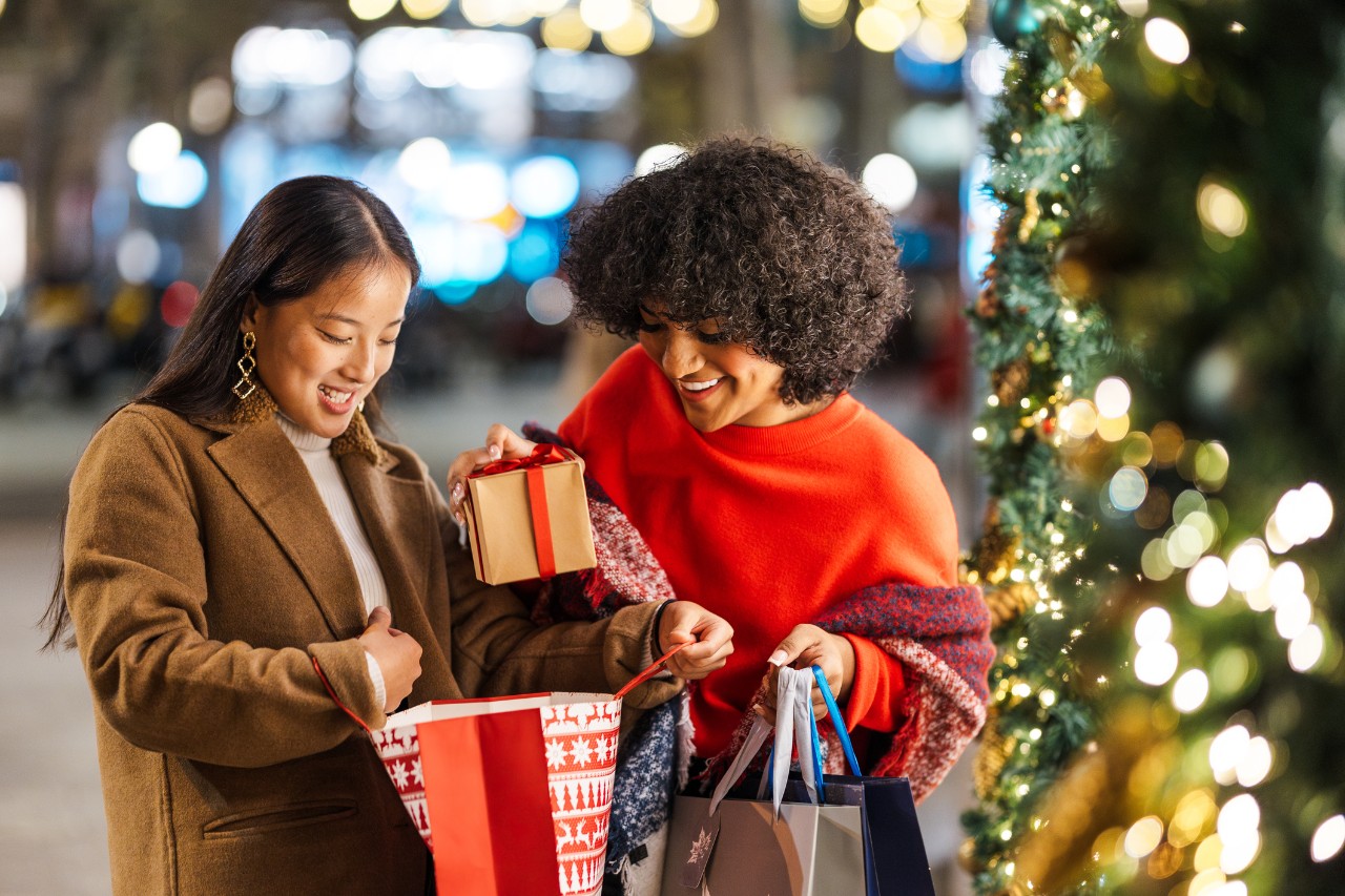 Two female friends are enjoying the christmas spirit by giving each other presents in a beautifully decorated city street
