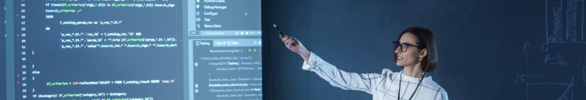 Profesora dando una clase mientras señala a una piarra en la  que muestra código