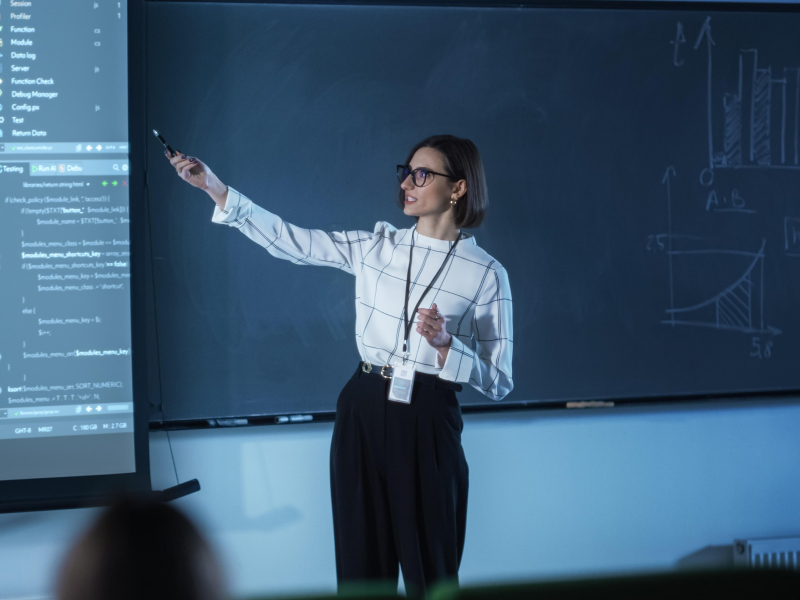 Profesora dando una clase mientras señala a una piarra en la  que muestra código