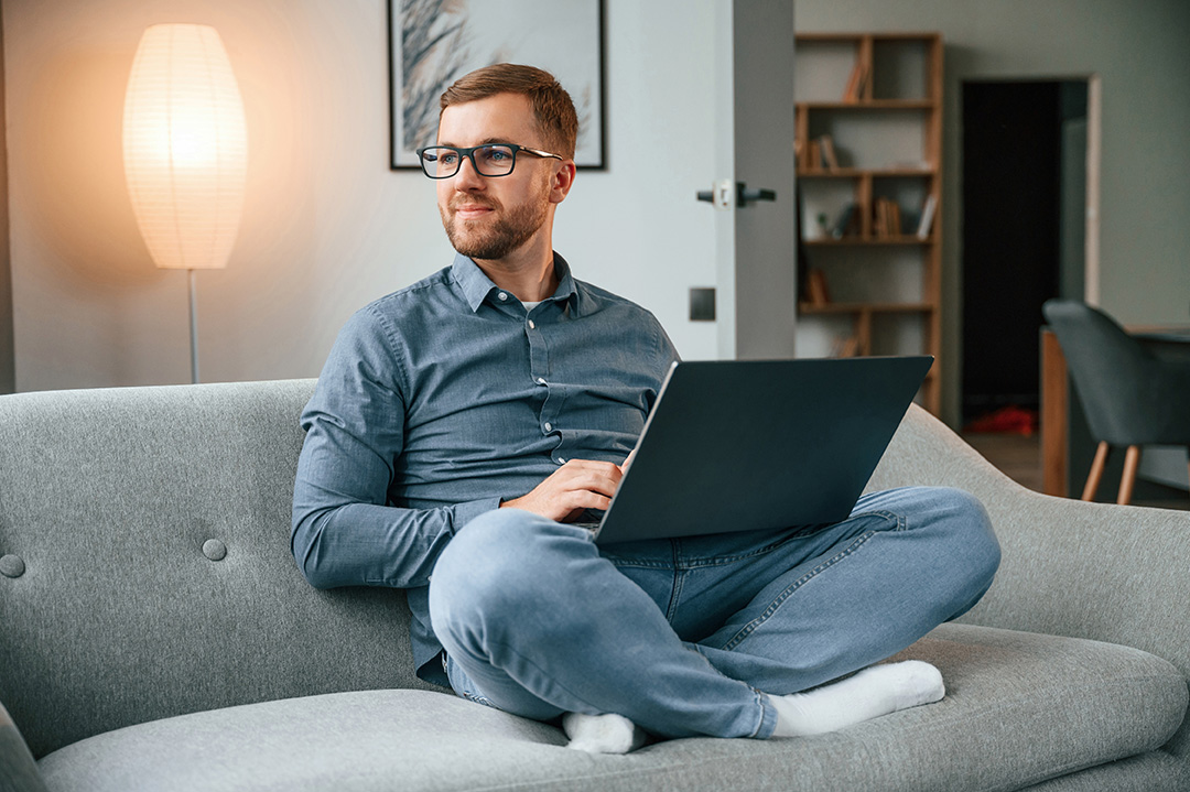 Male freelance worker in glasses is using laptop at home. Cozy apartment.