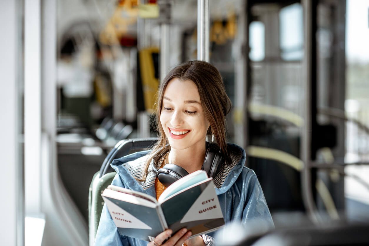 uma estudante sentada no ônibus, com o fone sobre os ombros, lendo um livro