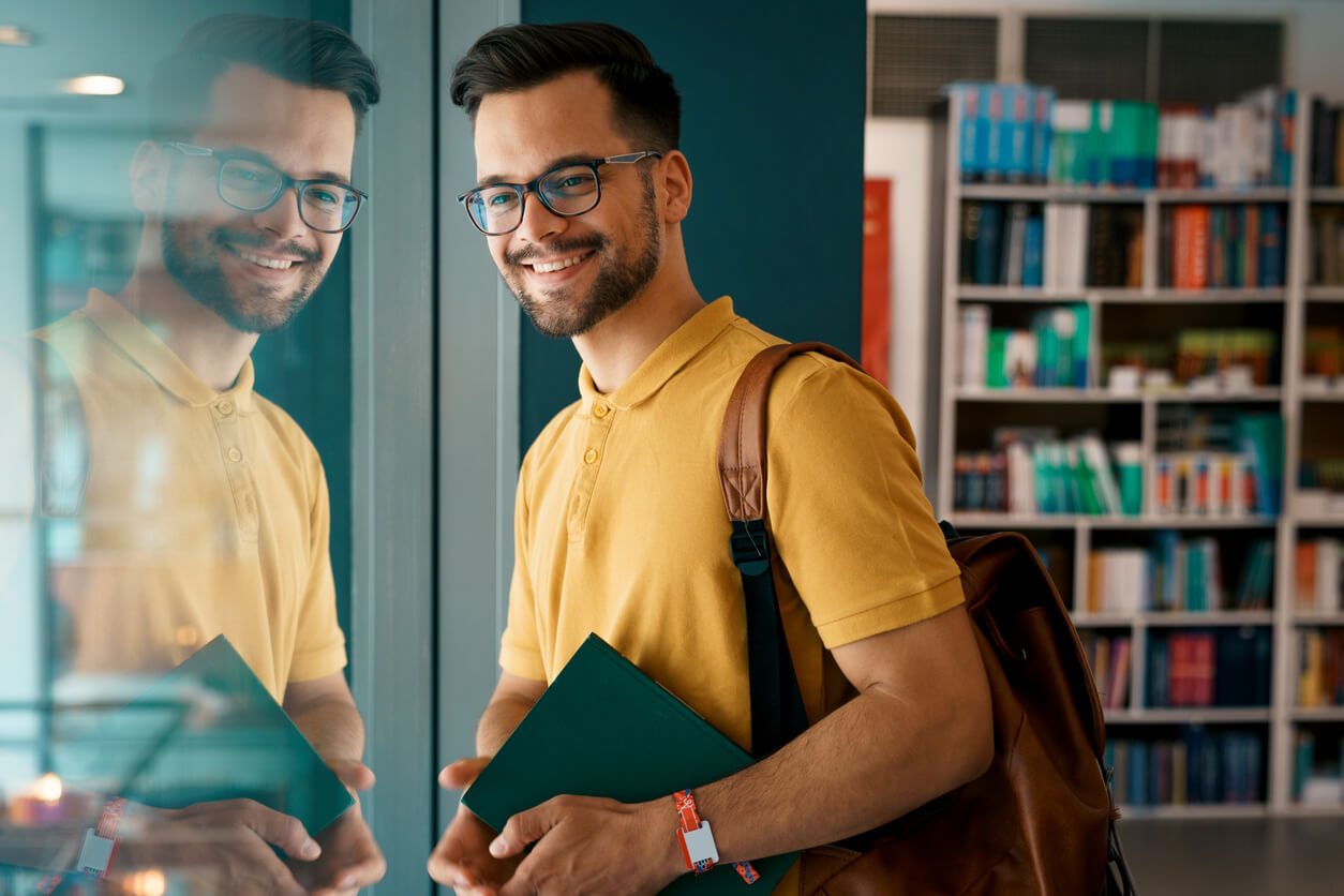 Jovem universitário na biblioteca contente por ser bolsista em um programa de permanência.  