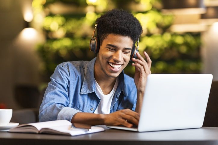 Aluno com fone de ouvido diante do computador e sorrindo porque estudar mudou sua vida