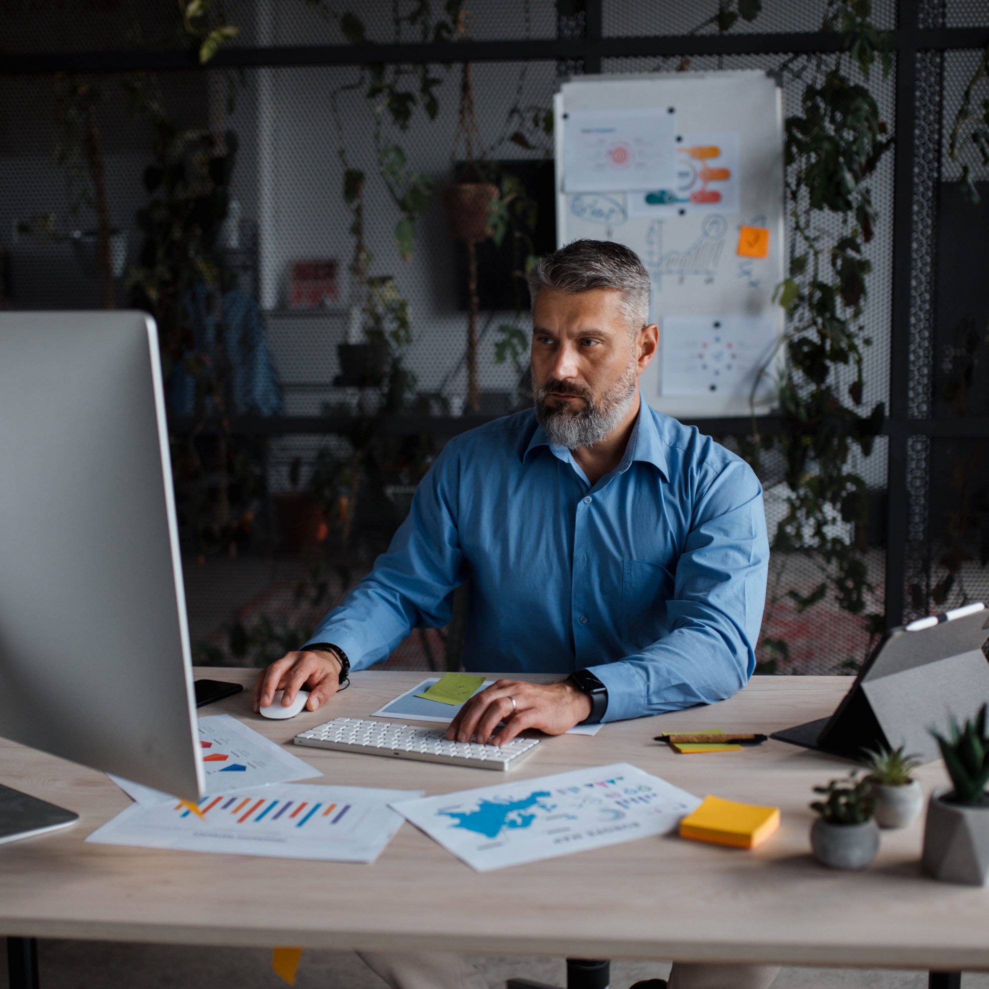 A white-collar worker is seated at a desk with a personal computer, surrounded by office equipment and supplies. A plant adds a touch of greenery to the workspace.