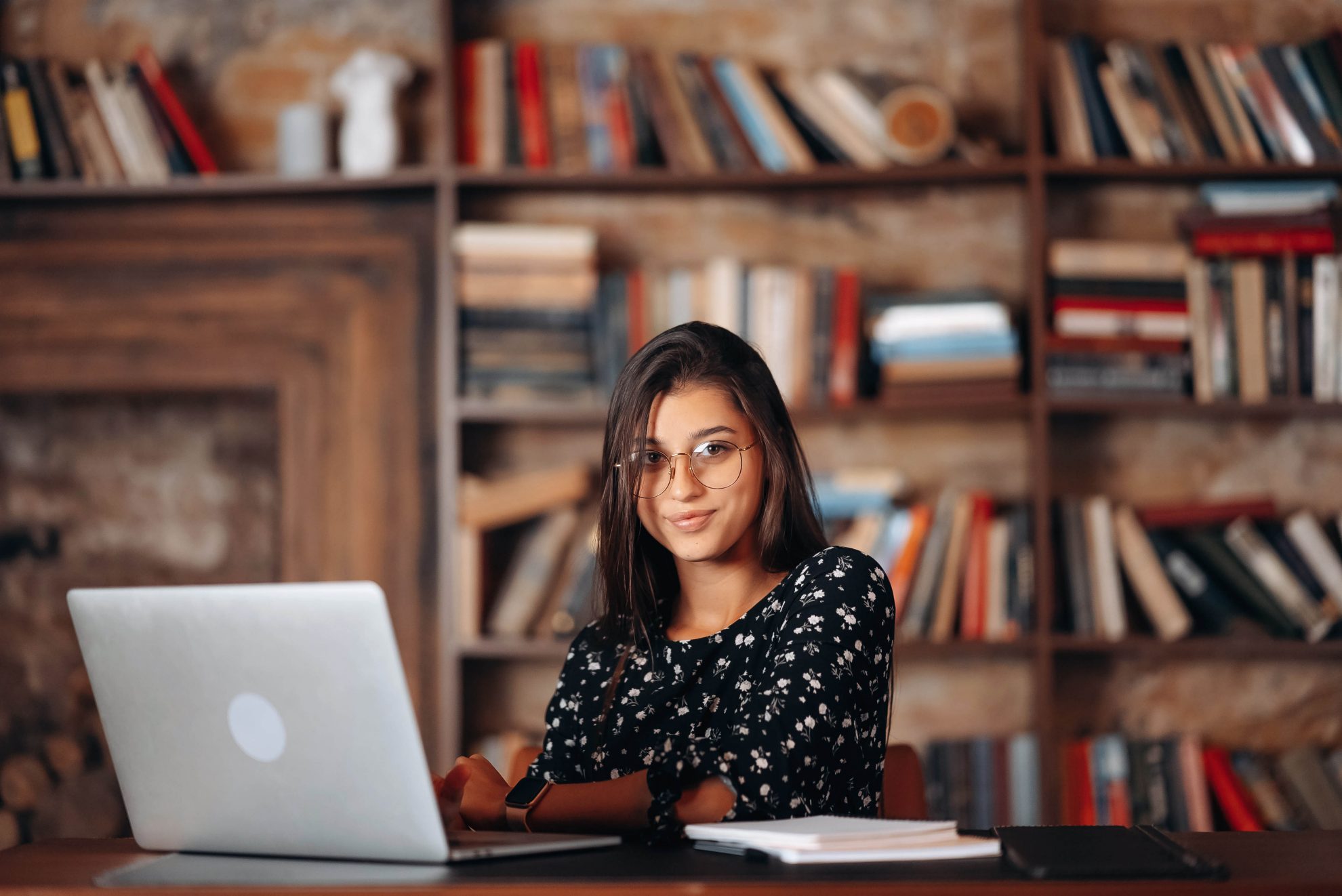 Young beautiful woman in glasses works at the laptop while sitting at the table